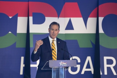 Ubrany w ciemny garnitur senator Rick Santorum przemawia na tle napisu CPAC Hungary